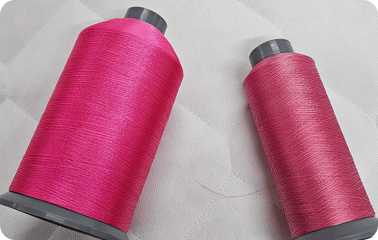 Two cones of pink quilting thread resting on white quilted fabric