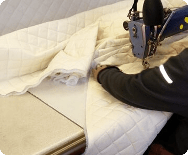 A machinist feeding cream quilted fabric through a sewing machine