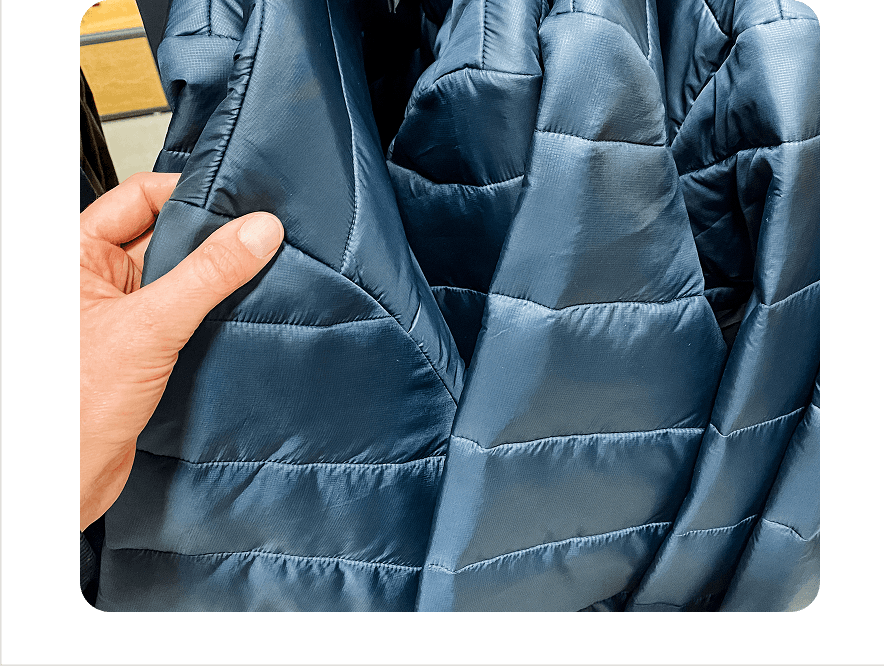 A hand holding the edge of a blue quilted jacket panel