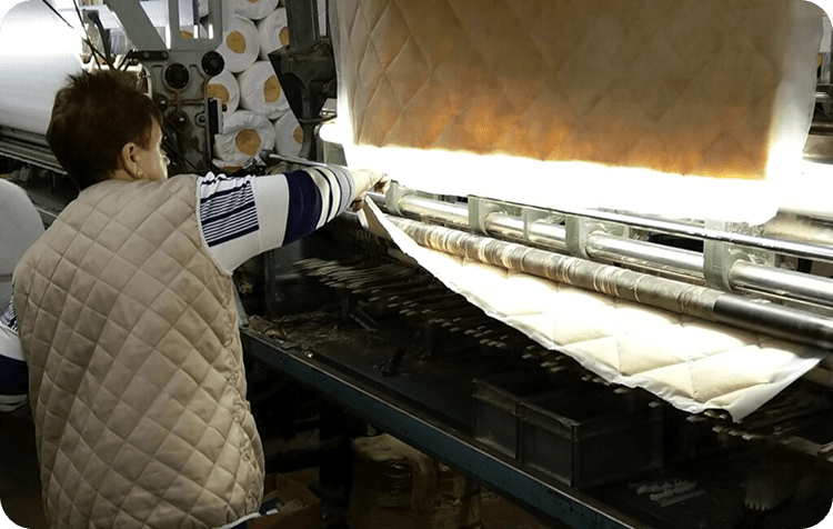 A machinist feeding cream quilted fabric through a wide quilting machine